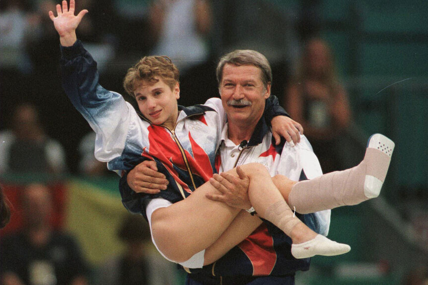 Coach Bela Karolyi carries an injured Kerri Strug to the medal ceremony after the US team win in artistic gymnastics.