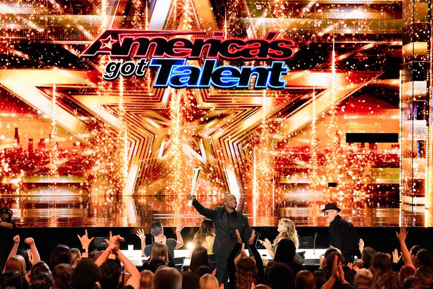 Terry Crews holds a large metal trophy on America's Got Talent Episode 1908.