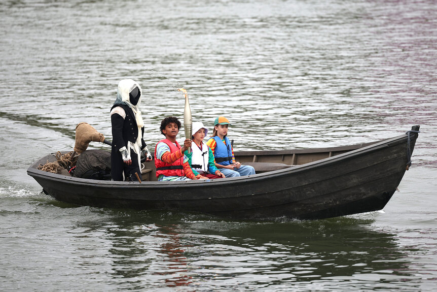 Children hold the olympic torch in a little boat for the 2024 olympics ceremony