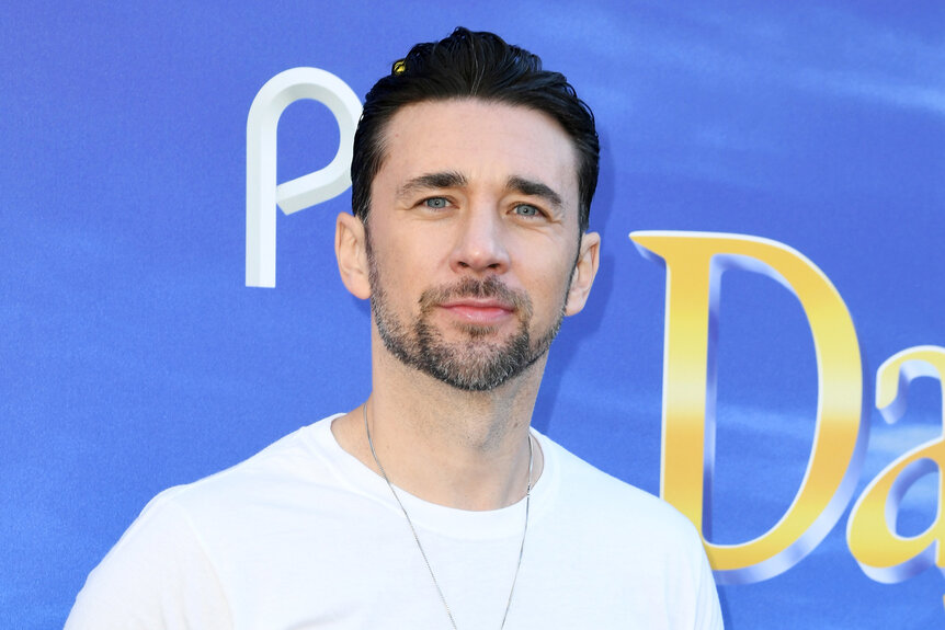 Billy Flynn smiles wearing a white shirt on the red carpet