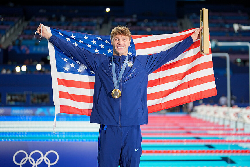 Bobby Finke holding up an American flag in front of a pool.