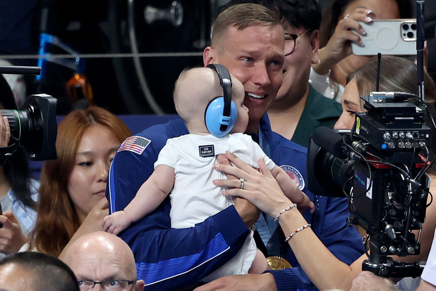 Gold Medalist, Caeleb Dressel of Team United States celebrates with his wife, Meghan Dressel (obscured), and his child, following the Medal Ceremony after the Men's 4x100m Freestyle Relay Final