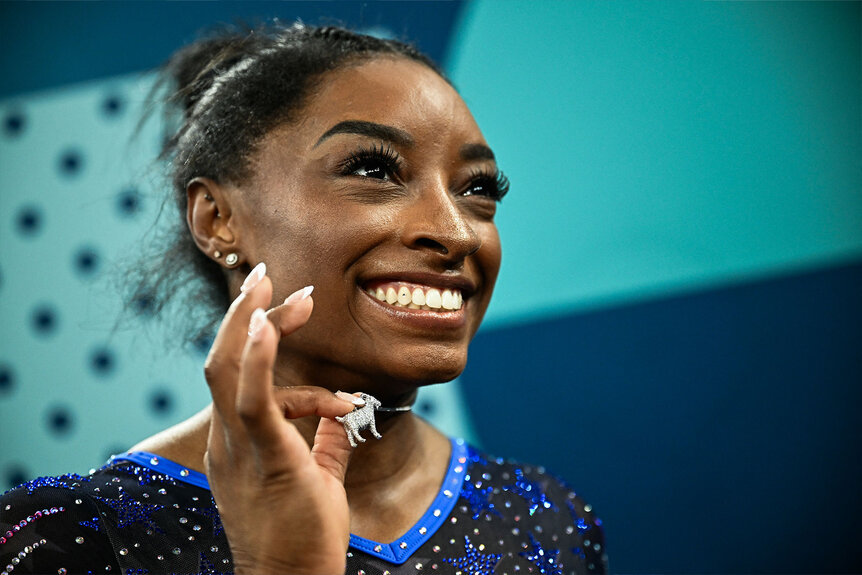 Simone Biles holds up her diamond goat necklace after winning the artistic gymnastics women's all around final of the Paris 2024 Olympic Games at the Bercy Arena in Paris, on August 1, 2024.