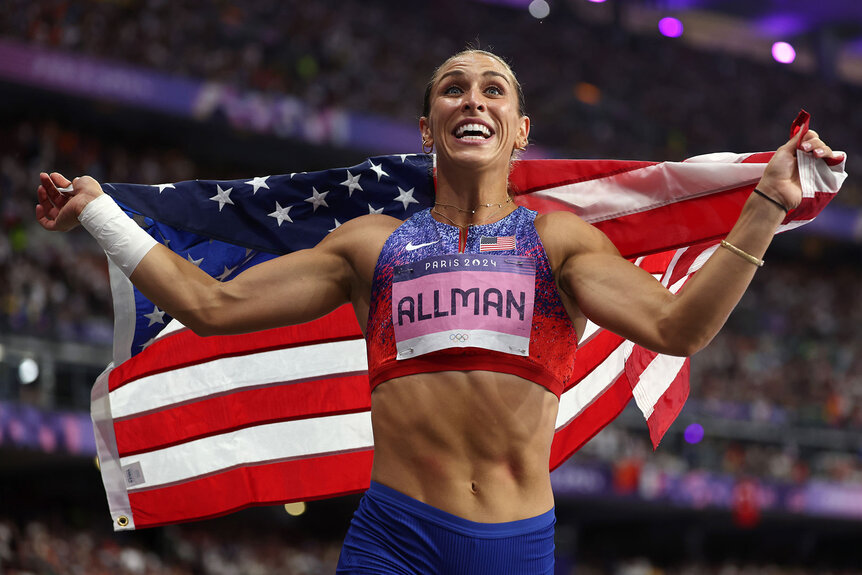 Valarie Allman smiling while holding the American flag at the Paris 2024 Olympics.