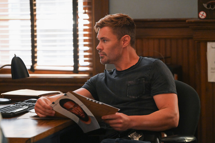 Adam Ruzek (Patrick Flueger) sits at his desk