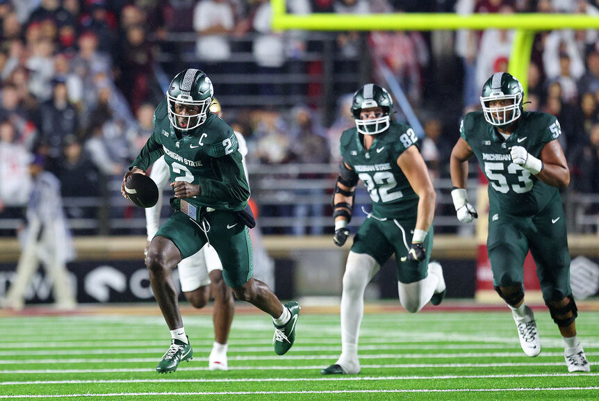 Aidan Chiles of the Michigan State Spartans running with a football on the field.