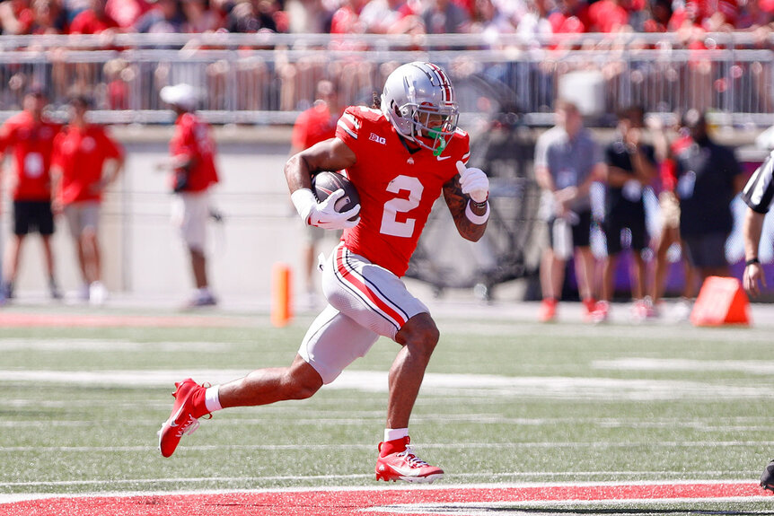 Emeka Egbuka of the Ohio State Buckeyes running with a football on the field.