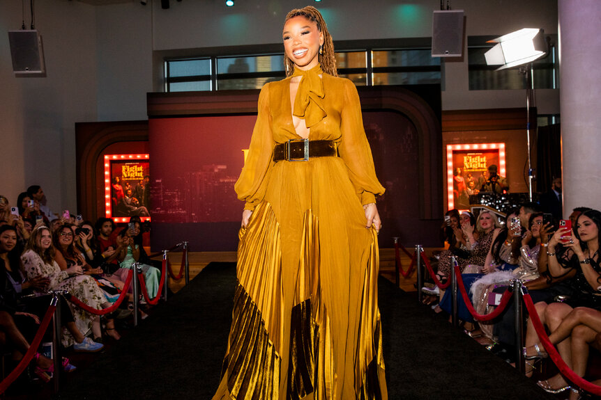 Chloe Bailey smiles in a golden yellow dress with a black belt