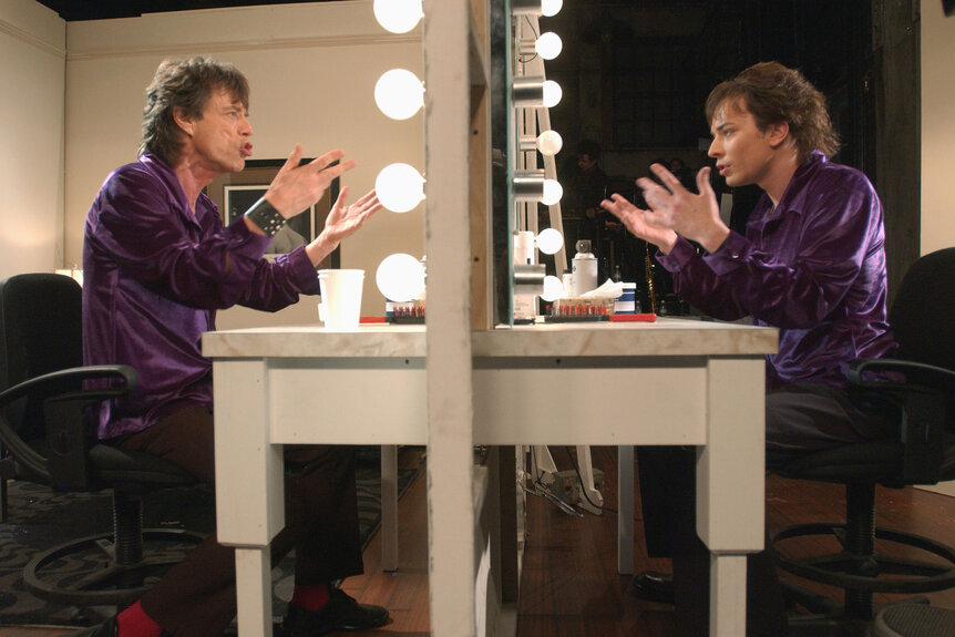 Mick Jagger sits as himself and Jimmy Fallon as Mick Jaggers reflection in an SNL skit