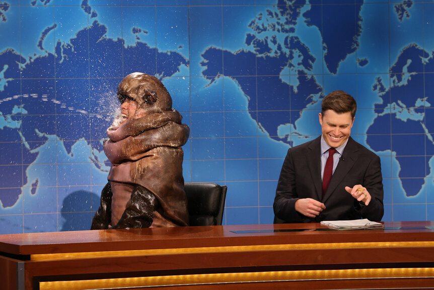 Bowen Yang dressed as a baby hippo gets sprayed with water next to Colin Jost on SNL