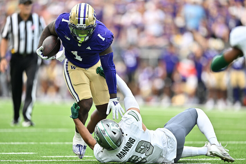 Jonah Coleman of the Washington Huskies runs the ball against Barry Manning of the Eastern Michigan Eagles