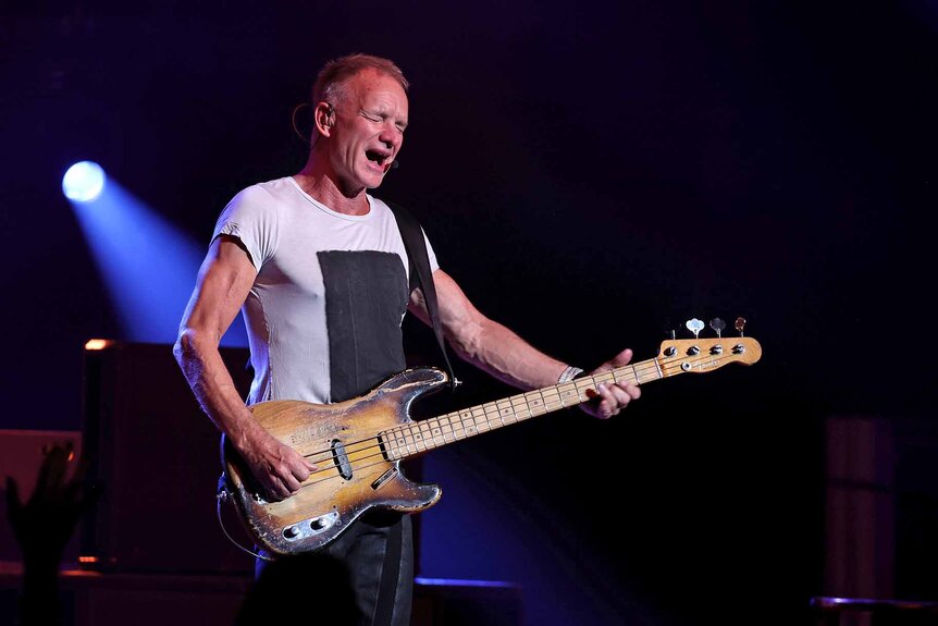 Sting plays the guitar and sings onstage.