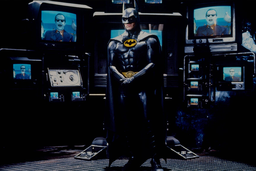 Michael Keaton staands in front of a bunch of televisions in Batman.