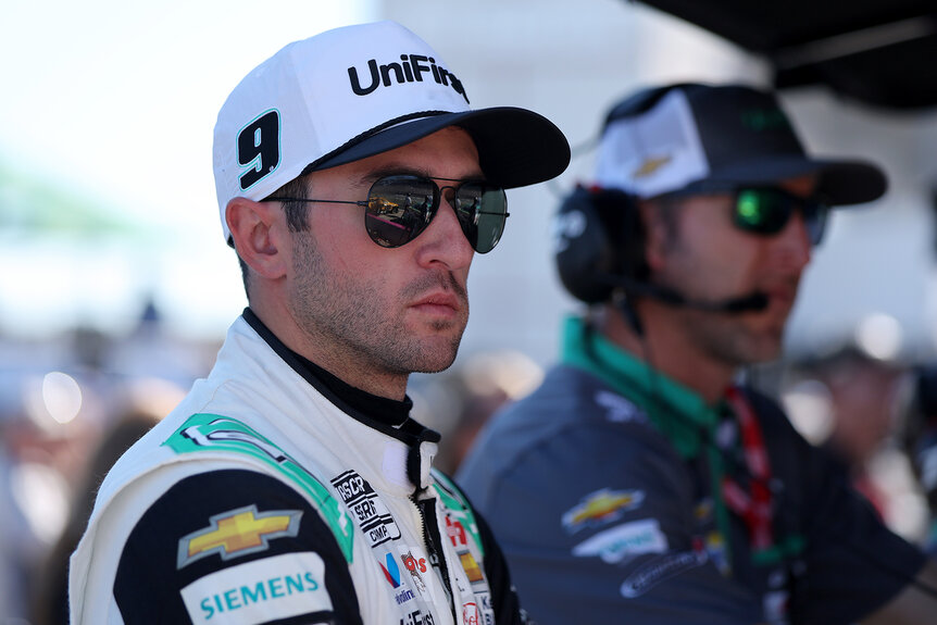 Nascar driver Chase Elliott looks on wearing sunglasses and a white hat during a race