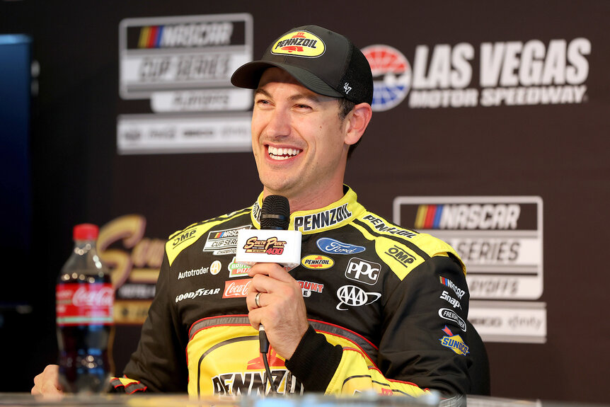 Nascar driver Joey Logano talks on a microphone in his uniform