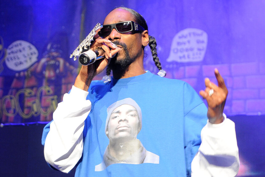 Snoop Dogg wears a large ring and a light blue shirt while performing on stage