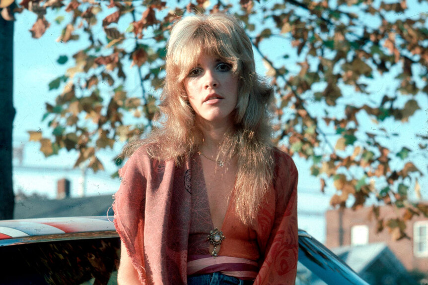 Stevie Nicks of Fleetwood Mac posed, sitting on car.