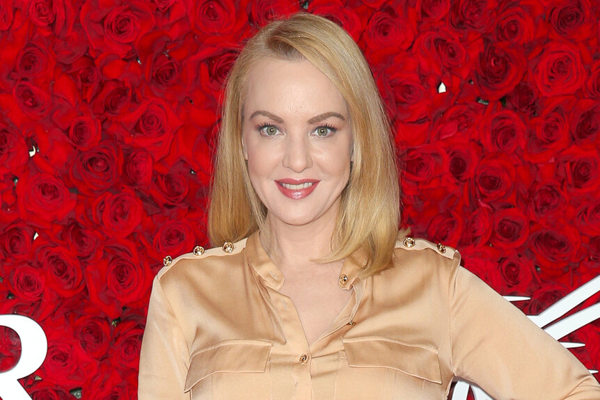 Wendi Mclendon-Covey wears a tan dress in front of a red rose backdrop