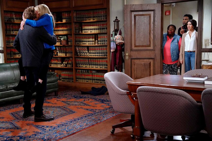 Jake (Ryan Hansen) and Abby Stone (Melissa Rauch) kiss as the cast watches in Night Court Episode 210.