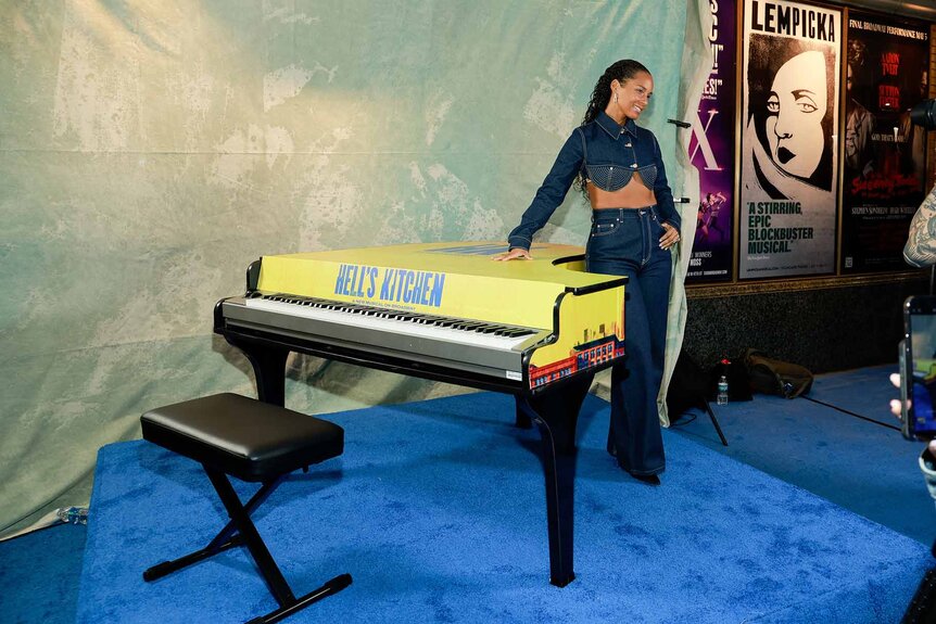 Alicia Keys poses next to a yellow piano.