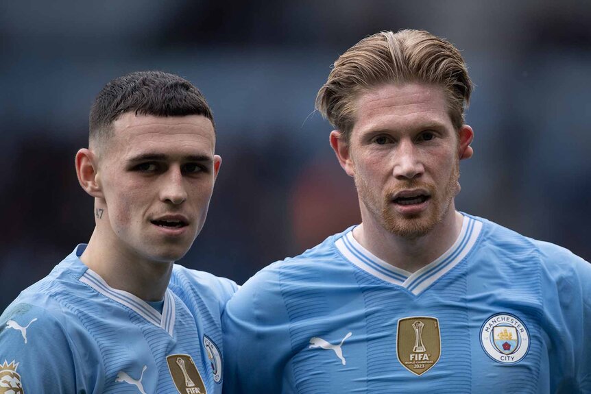 Phil Foden and Kevin De Bruyne of Manchester City stand together in their blue jerseys.