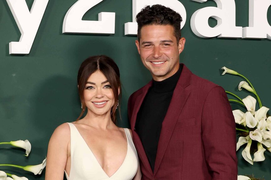 Sarah Hyland and Wells Adams pose together in front of a green backdrop.