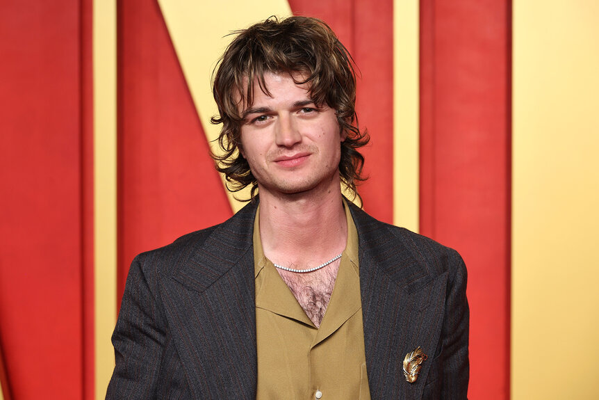 Joe Keery wears a mustard colored shirt and brown blazer on the red carpet