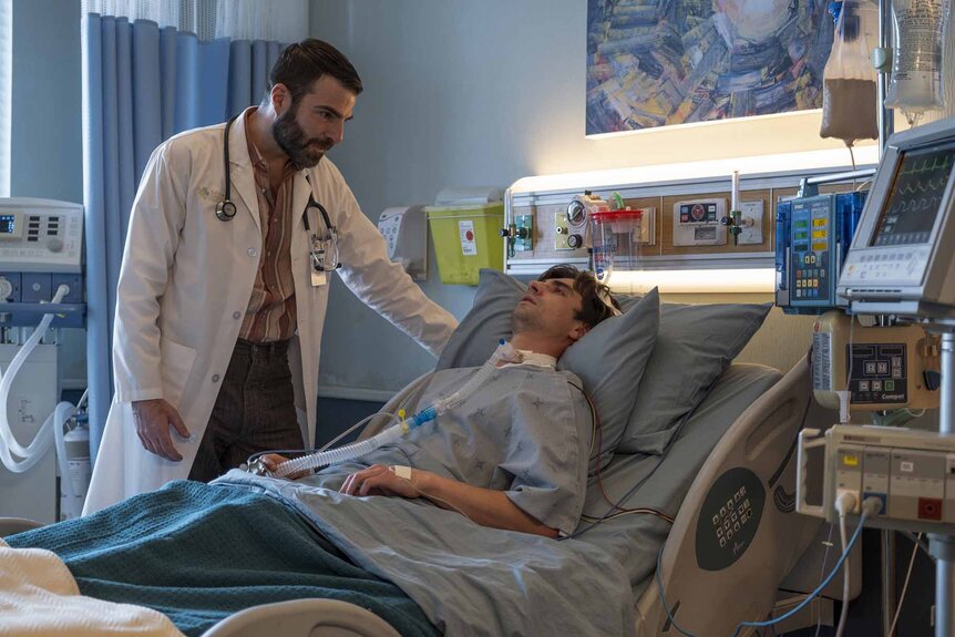 Dr. Oliver Wolf (Zachary Quinto) looks at Roman (John Doe) (Alex Ozerov-Meyer) in a hospital bed in Brilliant Minds Episode 107.