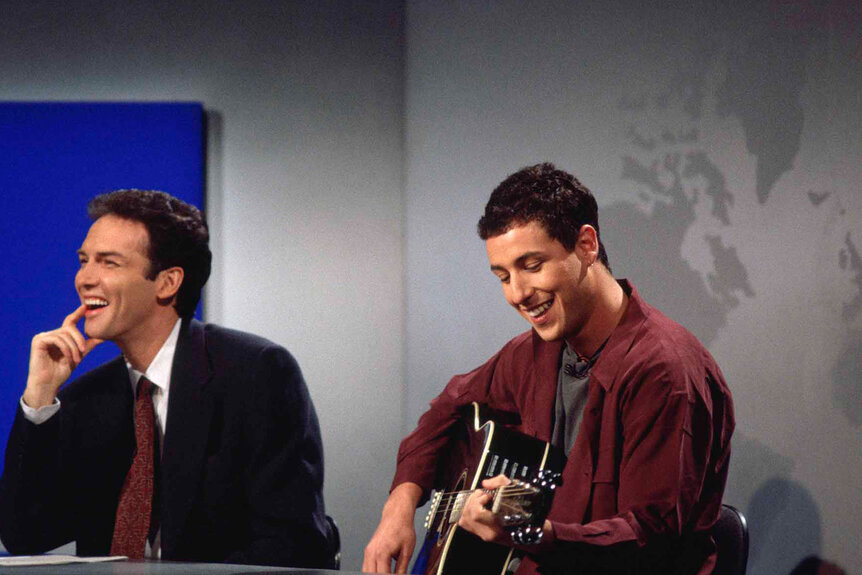 Norm MacDonald laughs as Adam Sandler plays the guitar on SNL..