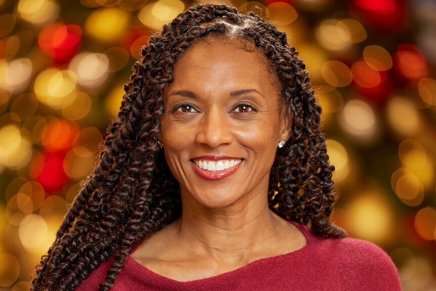 Danielle Reyes smiles in a red sweater in front of lights