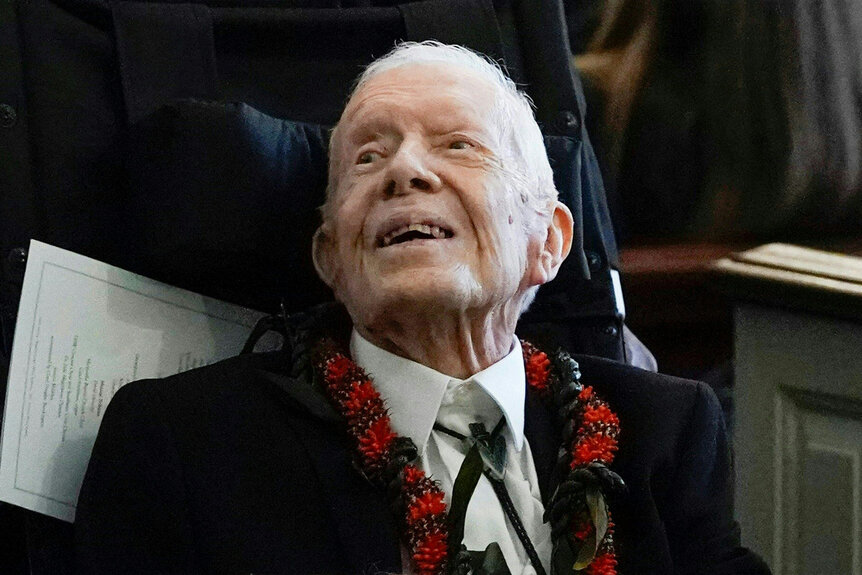 President Jimmy Carter smiles in a suit with a red flower necklace.