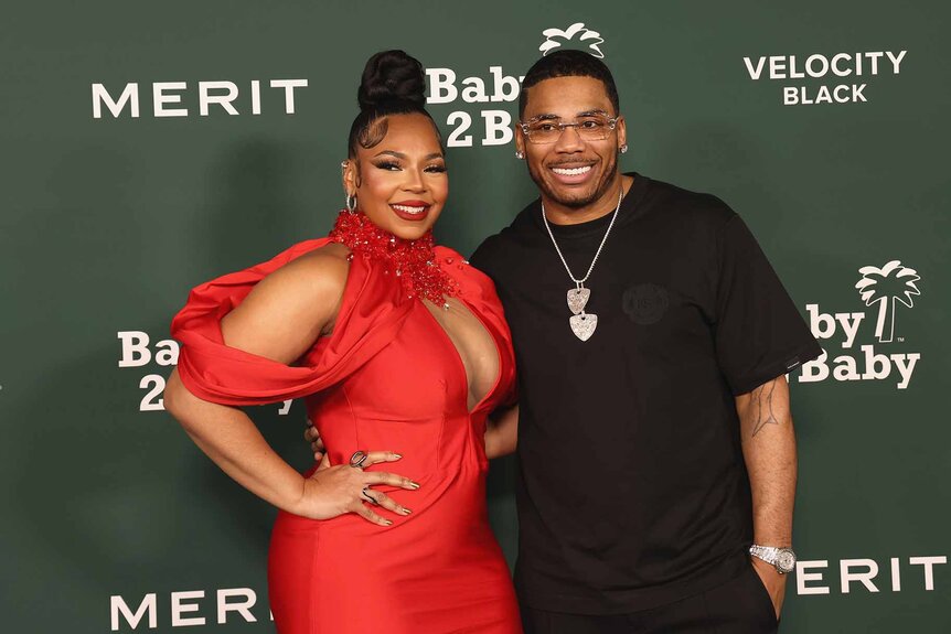 Ashanti and Nelly smile together in front of a green backdrop.