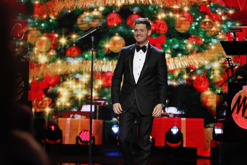 Michael Buble smiles in a tuxedo in front of Christmas decorations.