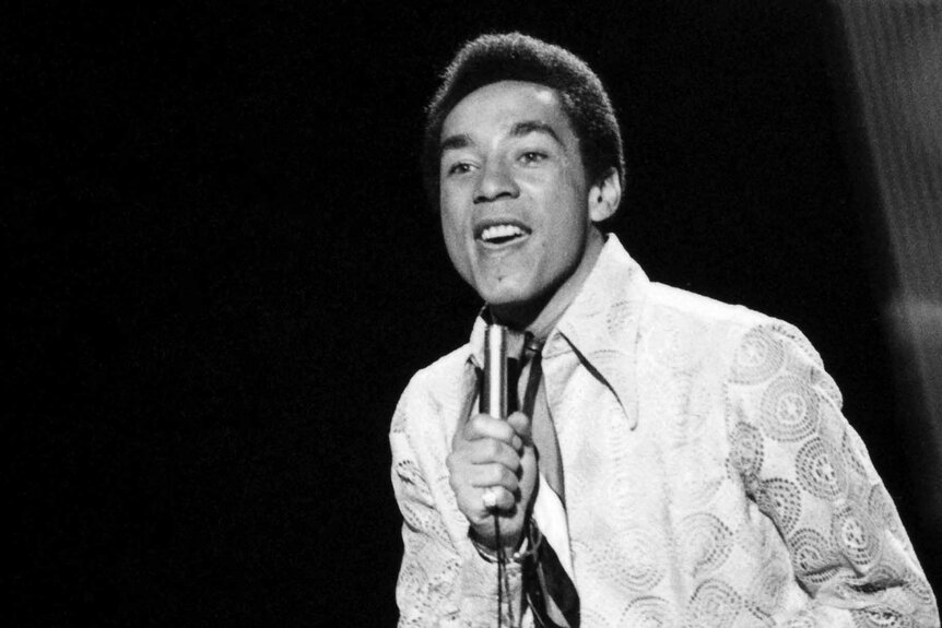 Smokey Robinson sings into a mic.