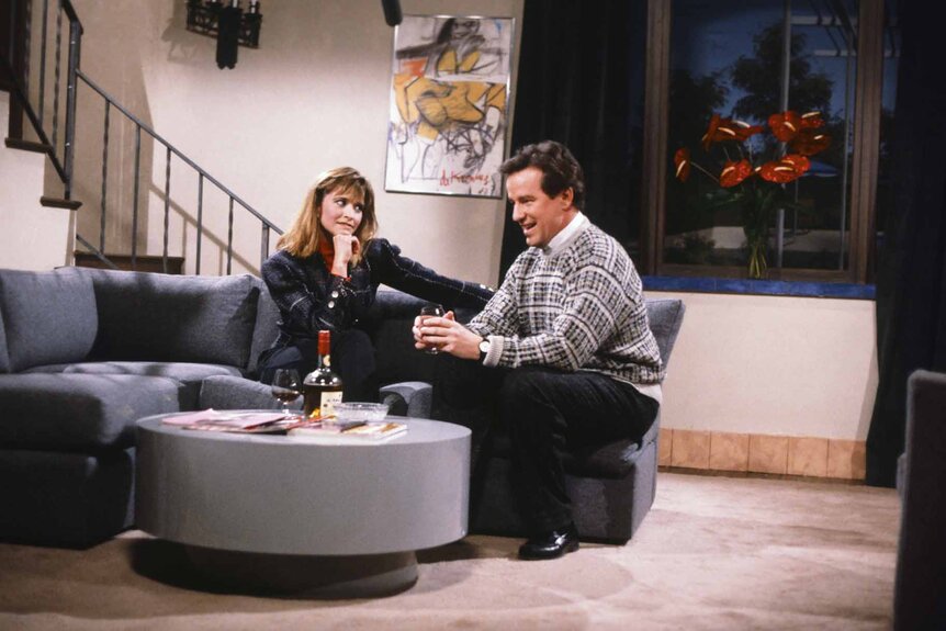 Leslie (Jan Hooks) and Dan (Phil Hartman) sit together on a couch during an SNL skit.