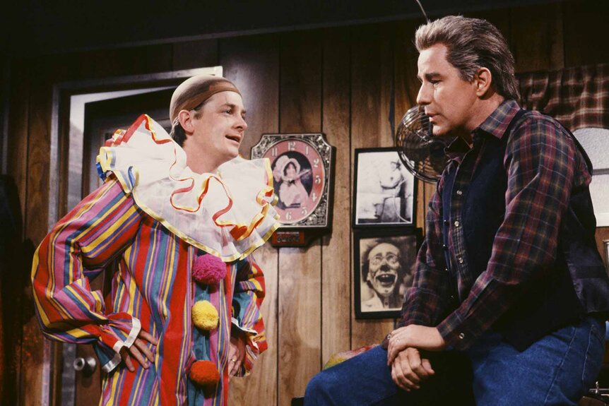 Jasper (Michael J. Fox) speaks to Mr. Chapman (Phil Hartman) while dressed like a clown during a sketch on SNL.