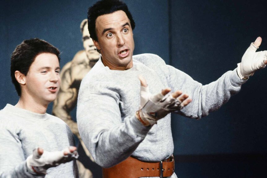 Hans (Dana Carvey) and Franz (Kevin Nealon) put their arms up in matching while uniforms on an SNL sketch.