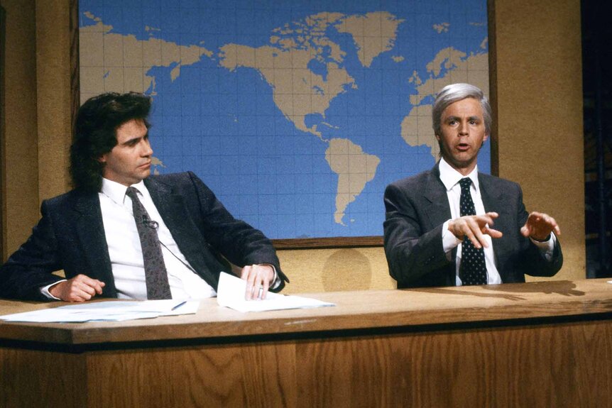 Dennis Miller and Jimmy Stewart (Dana Carvey) sit at the Weekend Update desk on SNL.