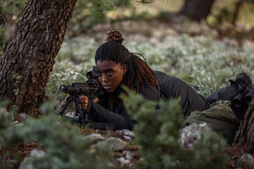 Bianca (Lashana Lynch) crouches on the ground an looks through a sniper rifle in The Day of the Jackal Episode 110.