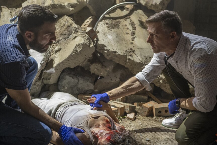 Dr. Josh Nichols (Teddy Sears) and Dr. Oliver Wolf (Zachary Quinto) tend to a wounded woman amongst rubble in Brilliant Minds Episode 112.