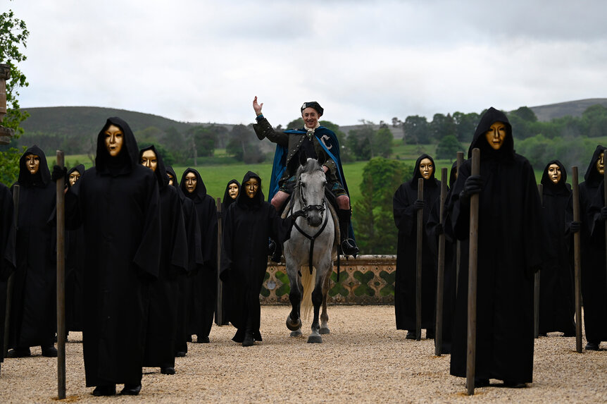 Alan Cumming on a horse at the castle walking through masked men on The Traitors Season 3 Episode 1