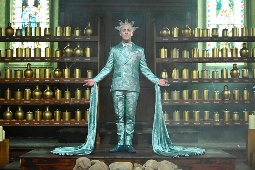 Alan Cumming wearing a teal sparkly outfit with a green cape and spikey headband on The Traitors Season 3, Episode 5.