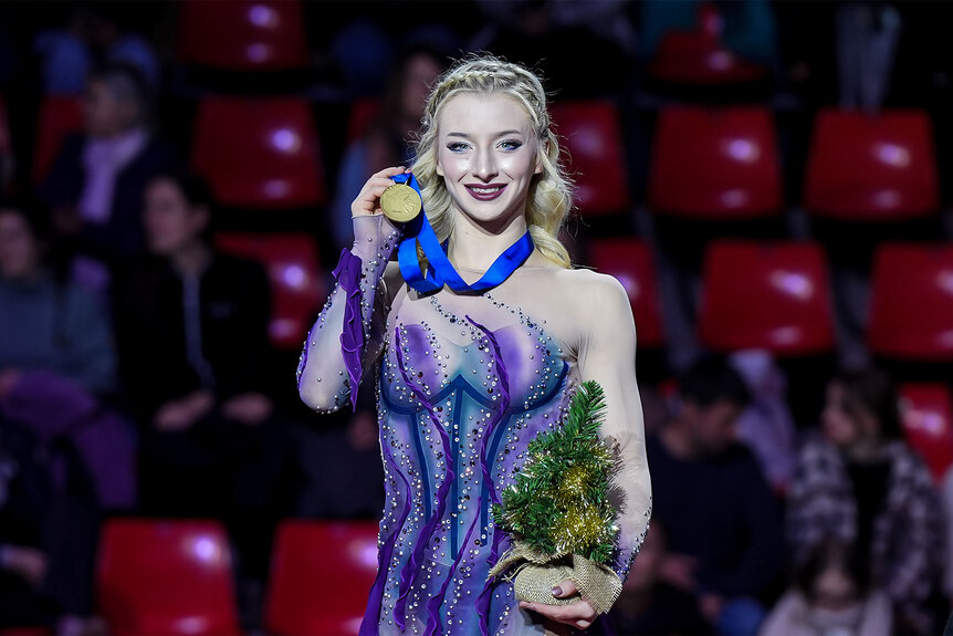 Amber Glenn smiling and holding up a medal.