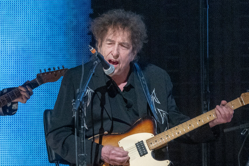 Bob Dylan performs on stage with a guitar during Farm Aid at Ruoff Home Mortgage Music Center