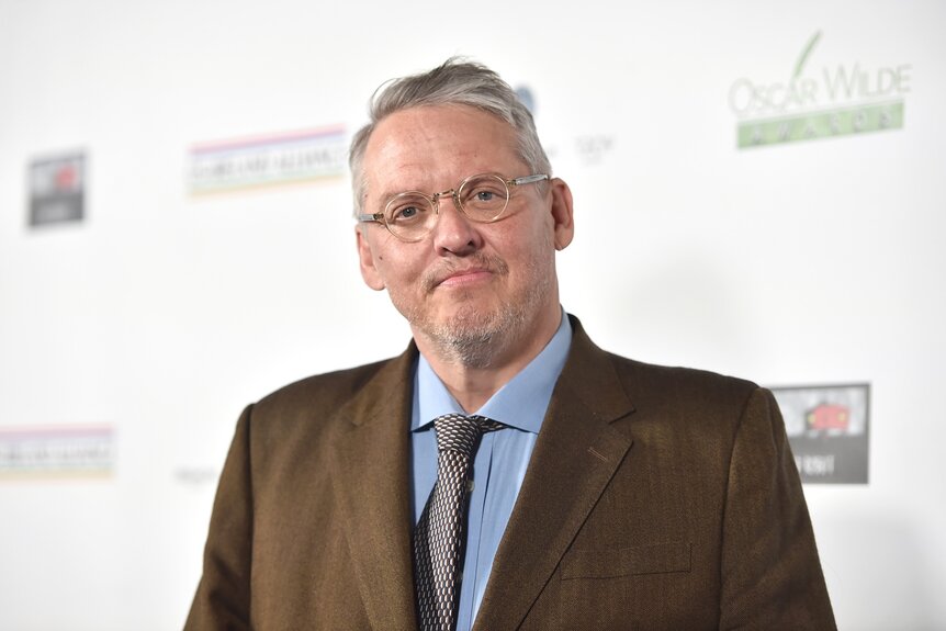 Adam McKay smiles in a brown suit with a blue shirt.