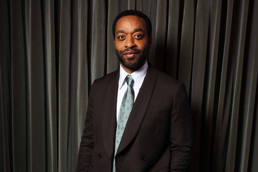 Chiwetel Ejiofor smiles in a suit and tie.