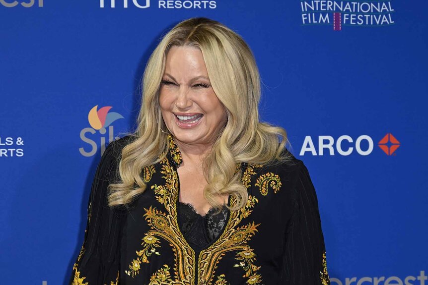 Jennifer Coolidge smiles in a black and gold top.