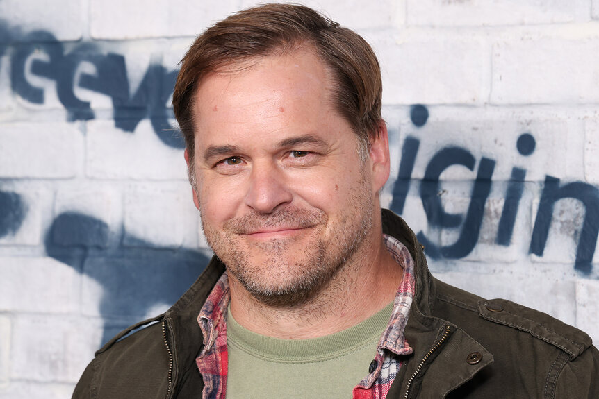 Kyle Bornheimer smiles in a green t-shirt at an event