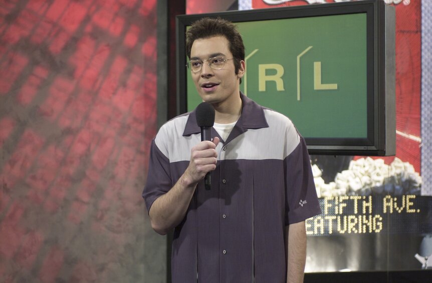 Carson Daly (Jimmy Fallon) speaks into a microphone on SNL Episode 2604.