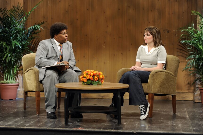 Clarence Jurnegan (Kenan Thompson) and Sarah Stokes (Casey Wilson) speak while sitting in two separate chairs on SNL Episode 1545.